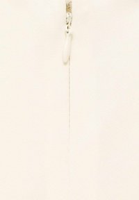 Tejido de punto en color crema con un cierre central y un tirador suave, así como costuras sutiles a lo largo de la costura, creando un diseño limpio.