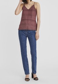 Top in cotone all'uncinetto bordeaux con scollatura a V, caratterizzato da motivi a strati e orlo ondulato, abbinato a jeans blu a vita alta e sandali neri.