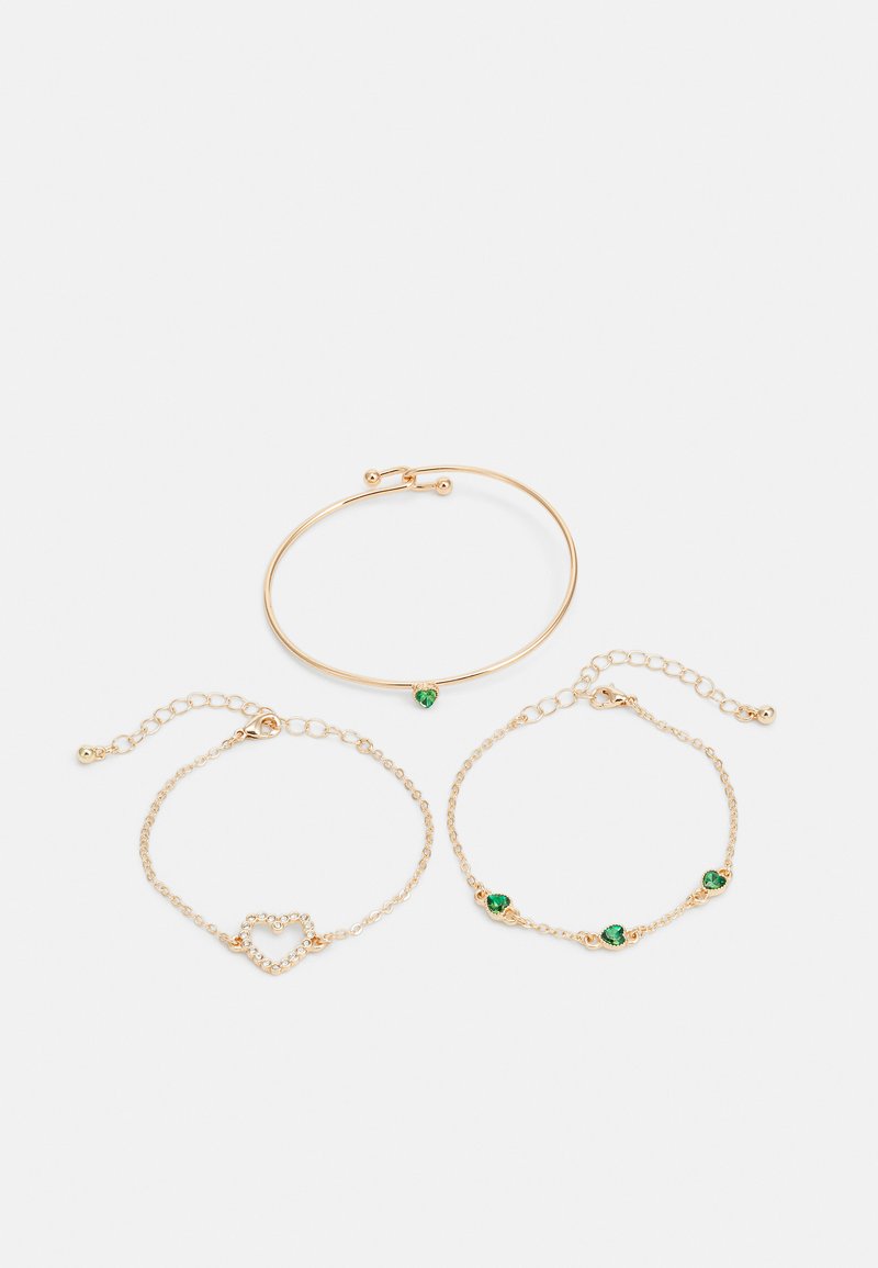 Set di tre bracciali color oro: un bracciale liscio, un bracciale a catena con contorno a forma di cuore, un bracciale a catena con accenti di gemme verdi.