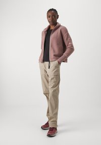 Fleece jacket in soft pink with a high collar, paired with beige cargo pants featuring pockets, and red hiking shoes with gray soles.