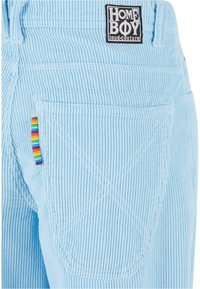 Pantaloni in corduroy blu con etichetta HOME BOY, una tasca posteriore e un piccolo tag a strisce arcobaleno sul lato per dettagli.