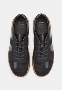 Svart läder- och mockaskor med en platt brun gummisula, mörka snören och en texturerad inredning. Har subtila varumärkesdetaljer.