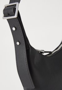 Borsa a tracolla in pelle nera con una texture liscia, hardware in argento, tracolla regolabile e dettagli di cucitura rinforzata.