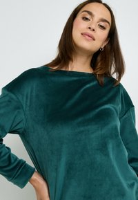 Top in velluto verde acqua con ampio scollo a barca, maniche lunghe e una consistenza morbida e liscia. Vestibilità comoda, senza motivi o dettagli visibili.