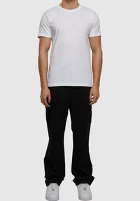 T-shirt blanc en coton avec un col rond, associé à un pantalon cargo noir avec des poches latérales, porté avec des baskets blanches.