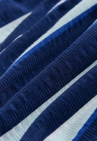 Sininen raidallinen kangas, jossa on vuorotellen tummia ja vaaleita sävyjä, tekstuurilla kudottu ja sileä pinta. Raidat vaihtelevat leveydeltään.