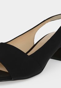 Μαύρο ανοιχτό παπούτσι slingback με χαμηλό χοντρό τακούνι και μπεζ εσωτερική επένδυση σε λευκό φόντο.