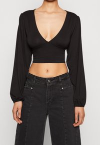 Svart kort topp med djup V-ringning och puffärmar. Tillverkad av mjukt tyg, har en figurnära design och slät yta.