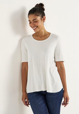 Hvid kortærmet top med rund halsudskæring og en afslappet pasform, lavet af letvægtsstof. Kombinationen med mørkeblå jeans.