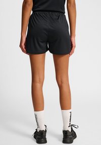 Svarta sportshorts med midjeband i elastiskt material, slät tygkvalitet och avslappnad passform. Kombineras med vita räfflade strumpor och svarta sneakers.