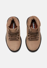 Hnědé kožené kotníkové boty s hnědými tkaničkami, polstrovaným límcem a gumovou podešví. Obsahují vyztužené švy a logo Timberland na stélce.