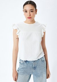 Top blanco de manga corta con bordes rizados y tela texturada, combinado con unos vaqueros de mezclilla azul claro. Diseño sencillo y casual.
