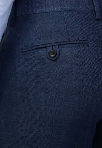 Pantaloni tailorati blu navy con una sottile texture a spina di pesce, tasca posteriore con un bottone nero e vita tailorata.