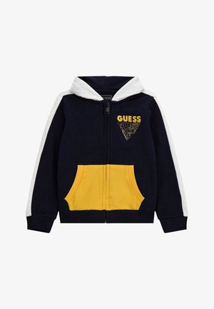 Námořnická modrá mikina na zip s bílou kapucí a pruhy na rukávech, žlutými předními kapsami a logem 'GUESS' v žluté barvě na hrudi.