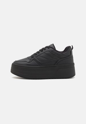 Czarny platformowy sneaker z grubą podeszwą, sznurowanym przodem, przeszyciami i wyściełanym kołnierzem na jasnym, jednolitym tle.