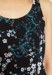 Top sin mangas negro con estampado floral que presenta flores blancas y rosas con ramas en tono teal. Tejido suave, escote redondo y diseño sin mangas.