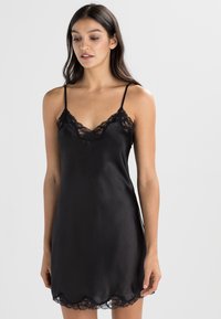 Vestido de satén negro con tirantes ajustables, borde de encaje y dobladillo ondulado, textura suave.