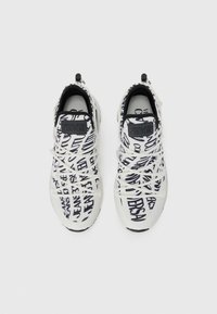 Hvite sneakers med et mønster som har svart tekst. Snøringene er hvite, med en svart logo på hælen. Runde tåform.