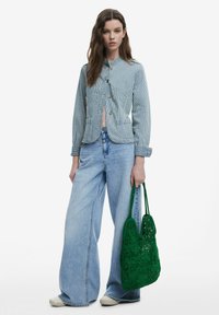 Randig denimjacka med en figurnära design, framstängning och två fickor, i kombination med vida ljusblå jeans och en grön virkad tote-väska.