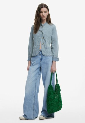Giacca di jeans a righe con vestibilità aderente, chiusura frontale e due tasche, abbinata a jeans a gamba larga blu chiaro e a una borsa a tracolla in cotone all'uncinetto verde.