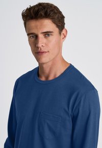 Blauw langemouw shirt van zachte stof, met een ronde halslijn en een borstzak met een subtiele textuur.