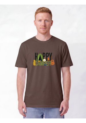 Homme portant un t-shirt marron avec des icônes de camping et le texte "Happy Camper", debout sur fond blanc.