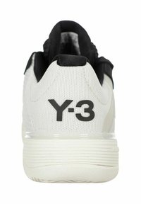 Sneaker bianco Y-3 con tomaia in tessuto testurizzato, dettagli neri e un logo nero prominente sul tallone. Design elegante con forma arrotondata.