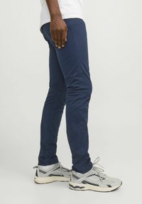 Námornícke modré slim-fit nohavice vyrobené z bavlnenej zmesi, s bočnými vreckami a hladkou textúrou, skombinované so šedými športovými teniskami.