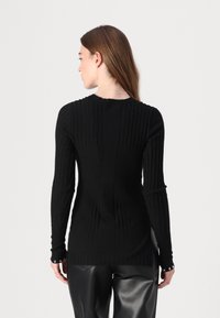 Pull long noir à côtes avec un col rond, présentant un tissu texturé et une silhouette ajustée, porté avec un pantalon en faux cuir taille haute.