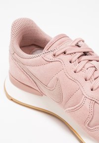 Růžové semišové tenisky s texturovaným síťovaným límcem, s jemným logem, tkaničkami a bílou mezipodešví, doplněné gumovou podešví.