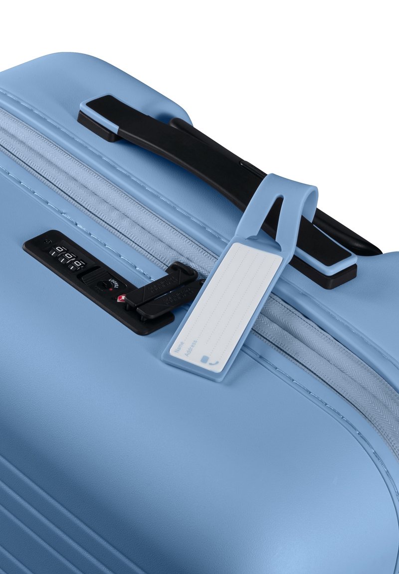 Valigia blu chiaro con manico nero, zip, lucchetto a combinazione integrato e etichetta per i bagagli bianca attaccata.