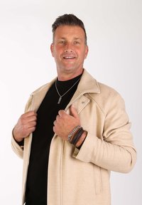 Beige wollen blazer met een geklapte kraag, gedragen over een zwart shirt; geaccessoireerd met gelaagd armbanden en een zilveren ketting.