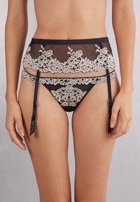 Sort blonde-strumpebælte med cremegul blomsterbroderi, parret med matchende nettrusse. Indeholder justerbare sorte satinbånd og blomsterdetaljer.