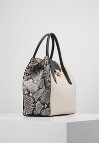 Stor handväska med en krämfärgad kropp, svarta läderdetaljer och en texturerad ormtryckt sida. Mjuk, strukturerad form med dubbla handtag.