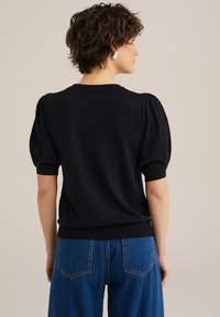 Svart stickad top med korta puffärmar, rund halsringning och ribbad nederkant. Matchas med blå högmidjade jeans som visar detaljer på bakfickorna.
