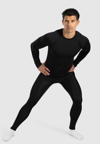 Musta urheilullinen pitkähiha, jossa on pyöreä pääntie ja tiukka malli, yhdistettynä mustiin kompressioleggareihin. Sujuva materiaali ja minimaalinen muotoilu.