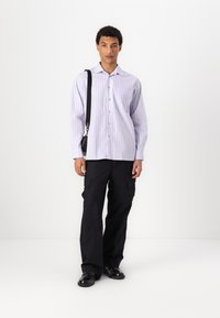 Light purple button-up shirt with vertical stripes, paired with black cargo pants. Model wears a black crossbody bag and black shoes.
