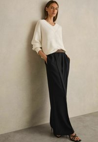 Maglione bianco lavorato a maglia con scollo a V, abbinato a pantaloni neri a gamba larga. L'outfit è completato da tacchi neri con cinturini.