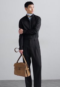 Cămașă neagră cu mânecă lungă și pantaloni cu guler înalt, asortați cu o geantă de umăr din suede bej. Țesătură netedă cu o siluetă ajustată.