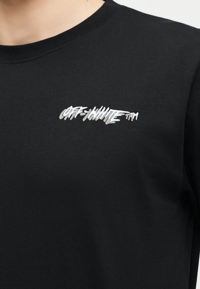 Μαύρο πουκάμισο με στρογγυλή λαιμόκοψη και μικρό λευκό και γκρι κείμενο "OFF-WHITE™" στην αριστερή πλευρά του στήθους, που φοριέται από ένα άτομο.