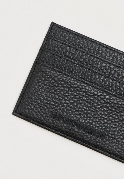 Porta-cartões em couro preto texturizado com o logótipo em relevo da Emporio Armani e múltiplos slots para cartões sobre um fundo claro.