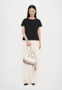 Svart kortermet topp med senkede skuldre, kombinert med høyt belte i kremfargede bukser og en gradient crossover-veske i beige og krem.