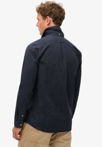 Donkerblauwe katoenen shirt met hoge kraag, lange mouwen en knoopaccenten; heeft een achterplooien voor extra comfort.