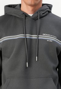 Sweatshirt à capuche gris avec cordons, poche avant, texte de logo blanc, et rayures horizontales bleues, vertes et noires sur la poitrine.