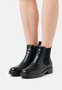 Bottines noires à motif crocodile texturé, avec des panneaux latéraux élastiques et une semelle épaisse en caoutchouc antidérapante.