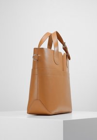 Tan leren tote bag met een gestructureerde vorm, dubbele handvatten aan de bovenkant en een gladde textuur. Voorzien van stikselaccenten en een vlakke bodem voor stabiliteit.