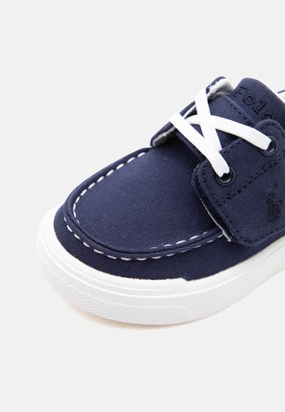 Καθημερινό παπούτσι από καμβά σε ναυτικό μπλε χρώμα με λευκά ραφτά, λευκά κορδόνια και χοντρή λευκή λαστιχένια σόλα, από μπροστινή όψη.