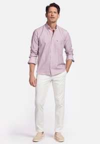 Chemise boutonnée à rayures rouges et blanches pour homme avec une poche poitrine, assortie à un pantalon blanc et des chaussures à enfiler beiges. Texture de tissu lisse.