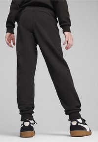 Černé tepláky s zúženým střihem, obsahující postranní kapsy a elastické manžety, doplněné černobílými teniskami s gumovými podrážkami.