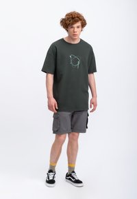 Donkergroen oversized t-shirt met een lichtblauw abstract patroon, gecombineerd met grijze cargo shorts en zwarte sneakers, met gele en grijze sokken.